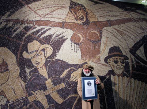 Nghệ sĩ Saimir Strati cầm bằng chứng nhận của Kỷ lục Guiness Thế giới trước bức tranh khảm cà phê khổng lồ.